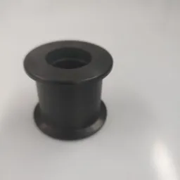 Czarny, metalowy element tulejowy z kołnierzem, wykonany na tokarce lub CNC, leżący na białym tle.