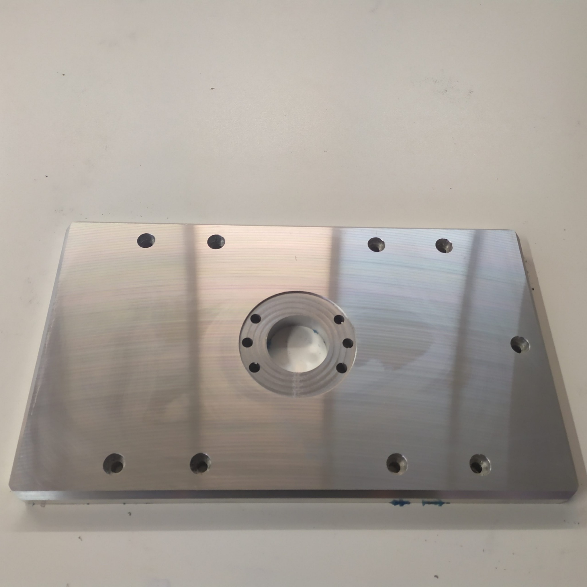 Płyta aluminiowa z wyfrezowanym otworem centralnym i otworami montażowymi, widoczne ślady obróbki skrawaniem.