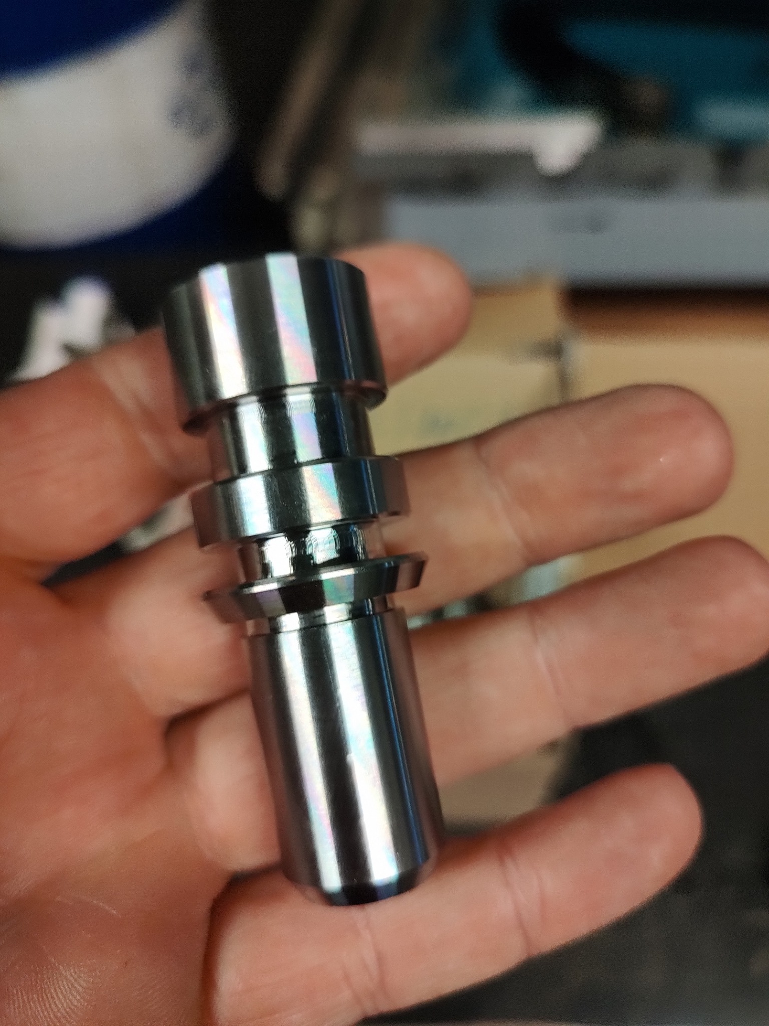 Precyzyjnie obrobiony, błyszczący, metalowy element w dłoni, widoczne ślady obróbki skrawaniem, wielostopniowa konstrukcja.