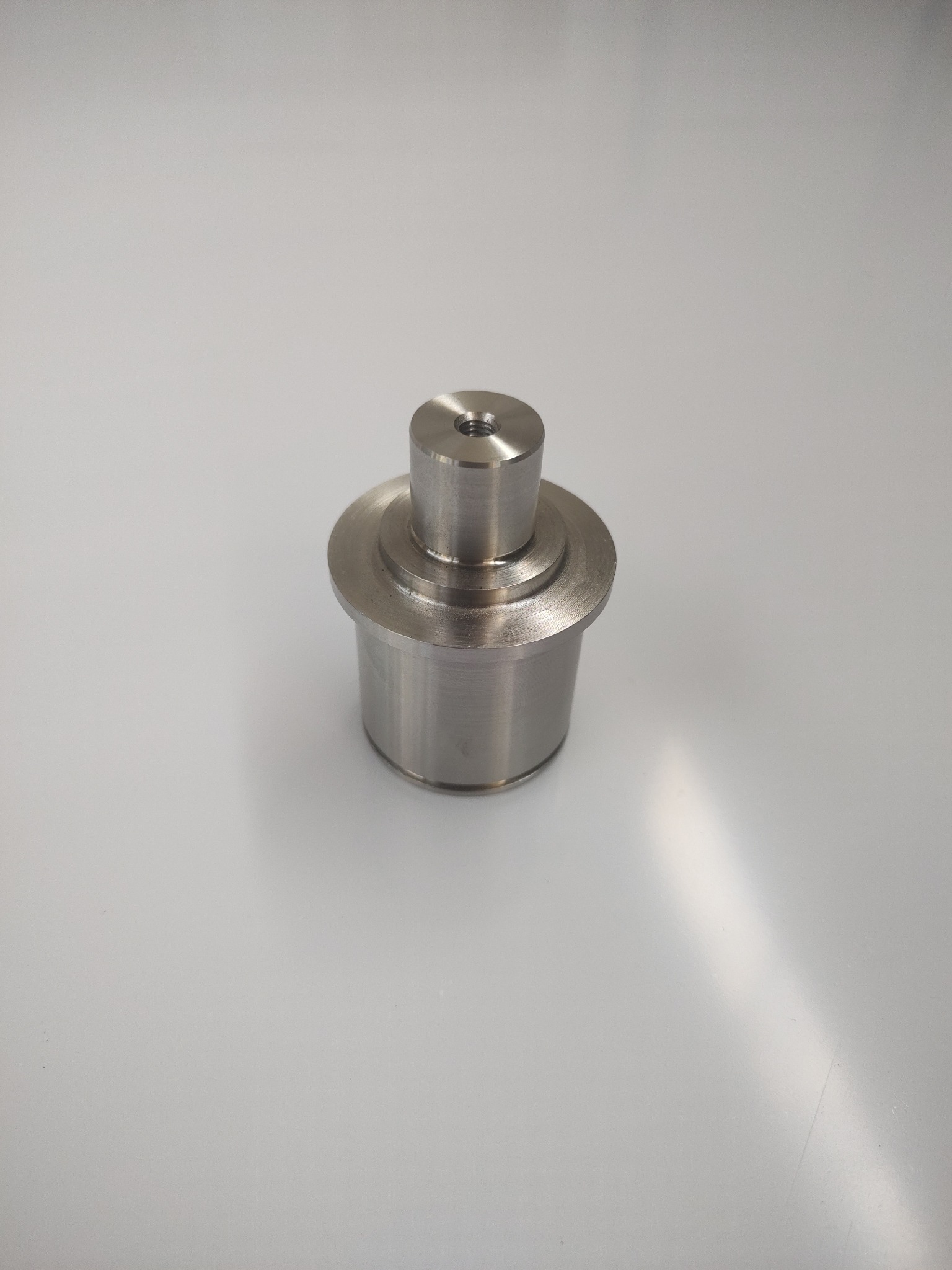 Metalowy element z otworem na górze, wykonany na tokarce lub obrabiarce CNC, leżący na gładkiej, jasnej powierzchni.