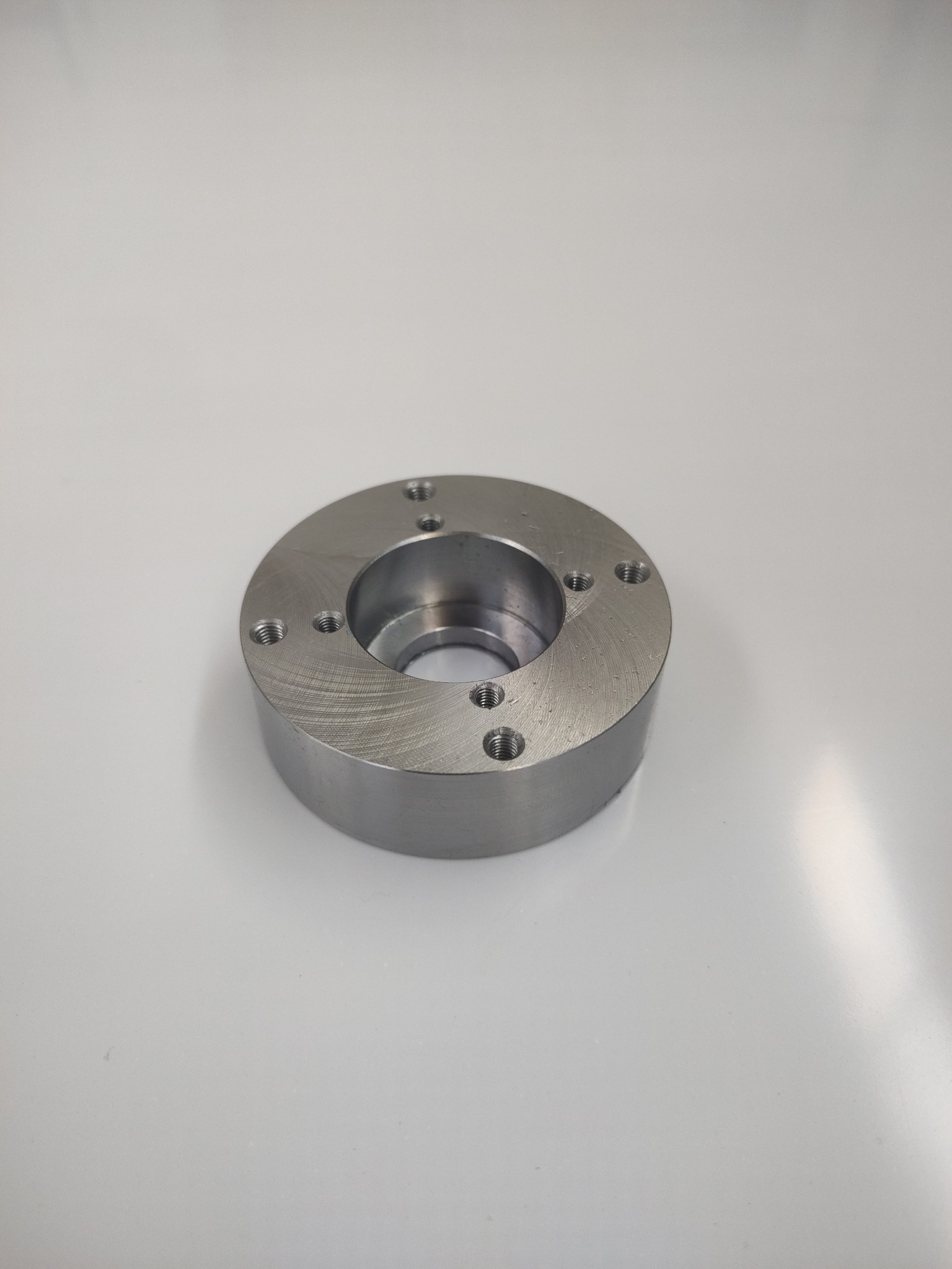 Metalowy pierścień z otworami, obrobiony na tokarce, leżący na białym tle. Widoczne ślady obróbki skrawaniem.