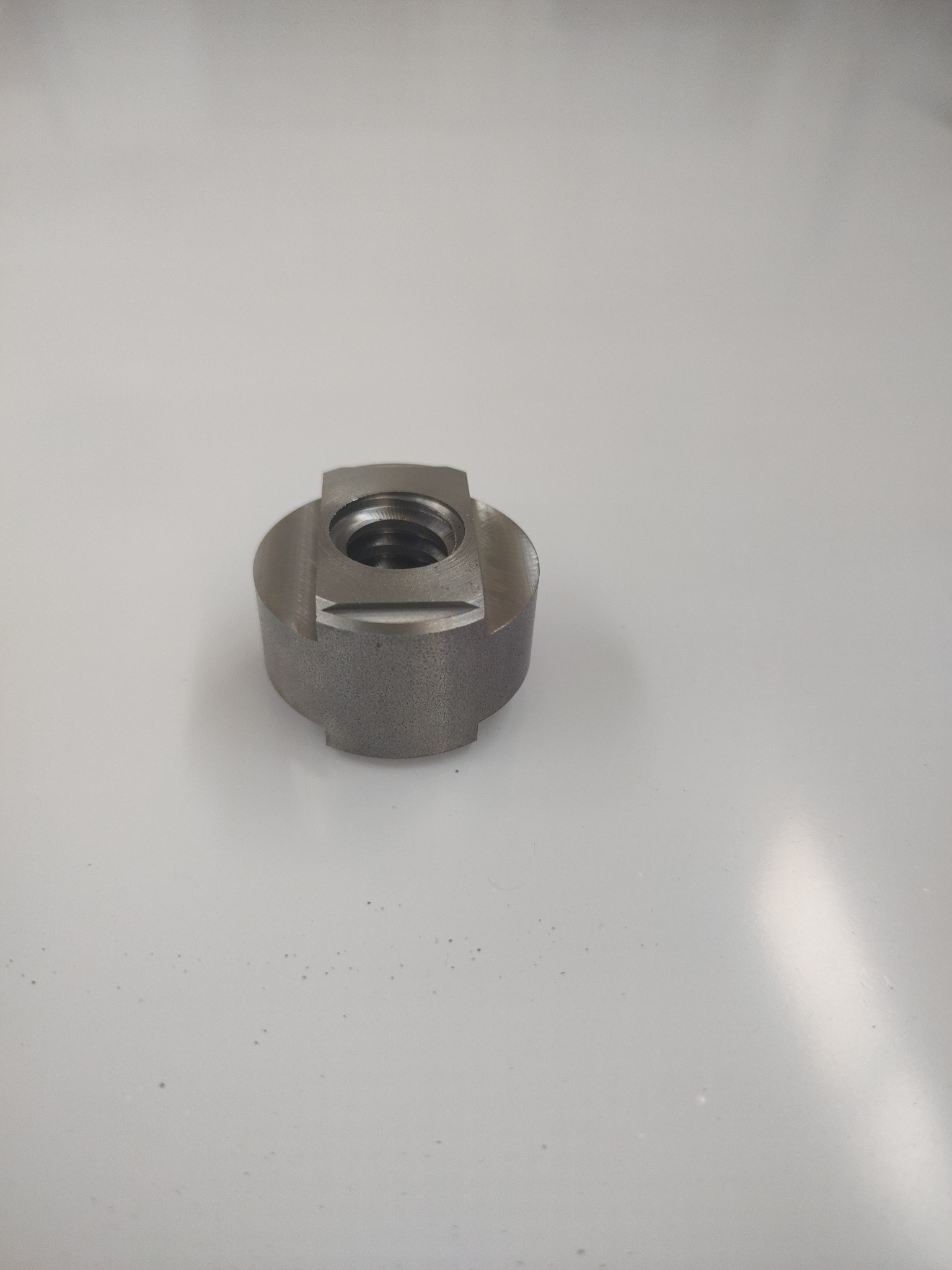 Metalowy, obrobiony element z gwintem wewnętrznym, leżący na białym tle. Widoczne ślady obróbki skrawaniem.