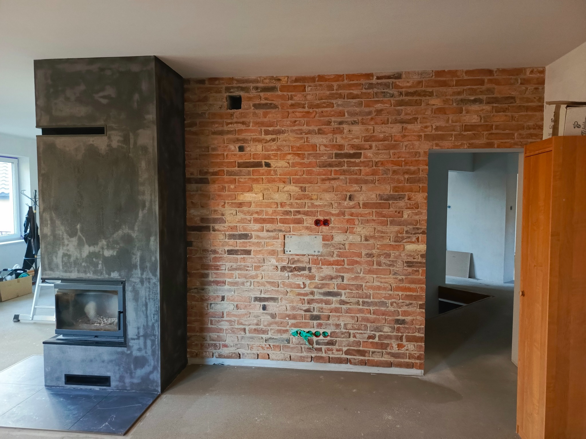 Ceglana ściana z instalacją elektryczną i kominek w surowym wykończeniu w trakcie prac wykończeniowych w Krosno.