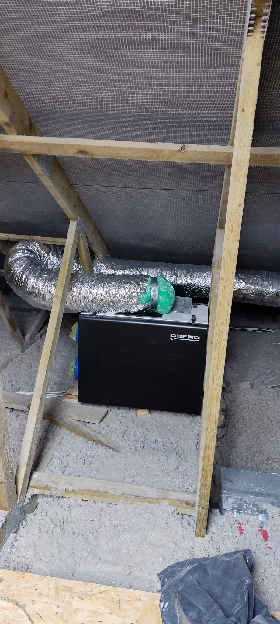 Czarny rekuperator DEPRO zamontowany na poddaszu, widoczne rury wentylacyjne, izolacja z wełny mineralnej i drewniana konstrukcja dachu.