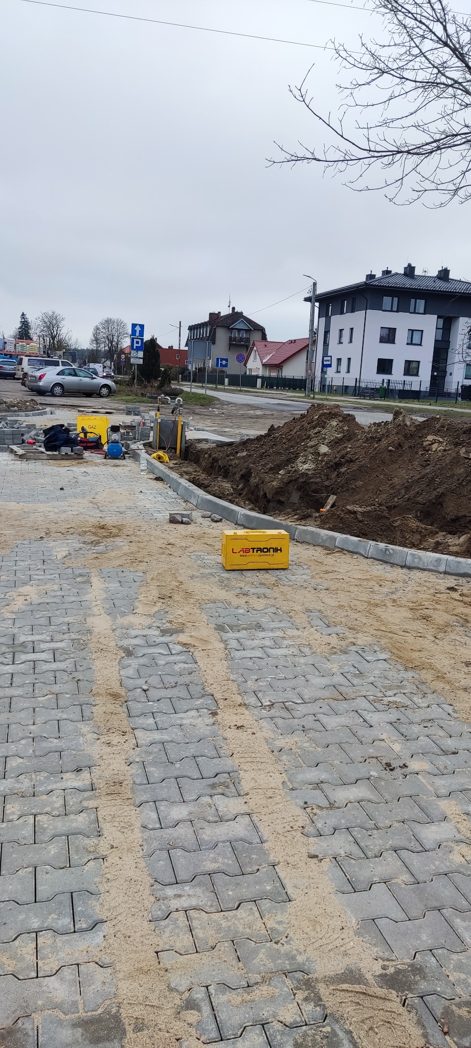 Prace ziemne i przygotowanie terenu pod instalację przyłącza, widoczny wykop, kostka brukowa, sprzęt do spawania gazowego oraz żółta skrzynka narzędziowa firmy Labtronik.