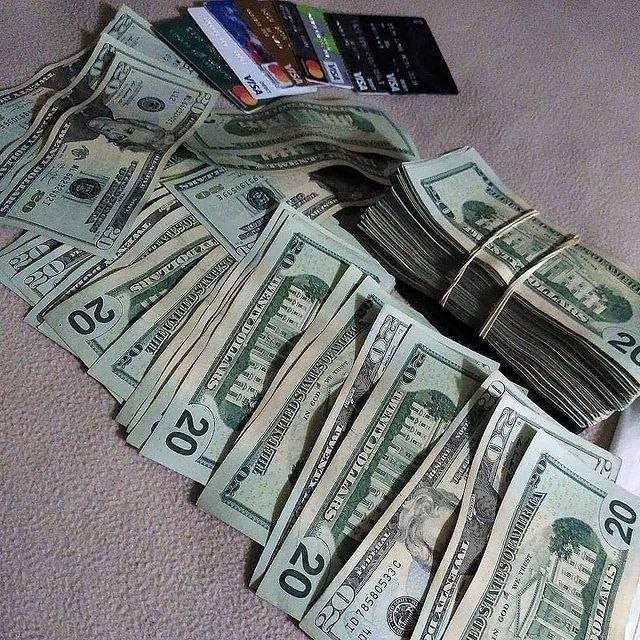 Stos banknotów dwudziestodolarowych z gumką i wachlarz kart płatniczych na teksturowanym tle.