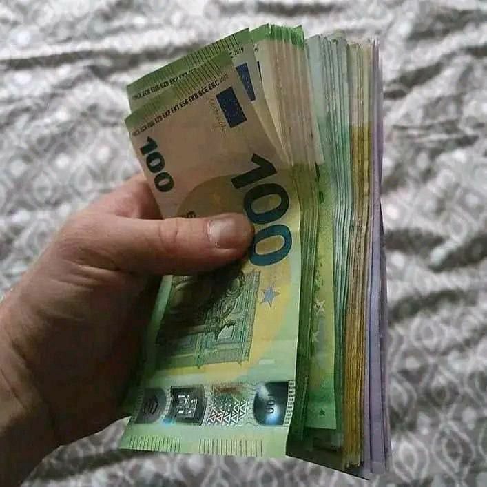 Dłoń trzymająca plik banknotów euro, widoczne nominały 100 euro, szare tło z wzorem.