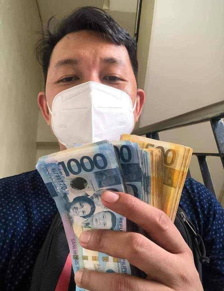Osoba w maseczce trzyma w dłoni plik banknotów filipińskich peso o nominałach 1000 i 500, widoczny numer seryjny SL739770 na jednym banknocie.