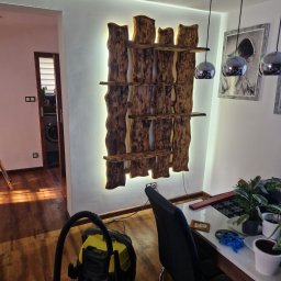 WULK-BUD - Drewniana, podświetlana półka o nieregularnych kształtach na białej ścianie, widoczna z perspektywy wnętrza, z elementami wyposażenia w tle.