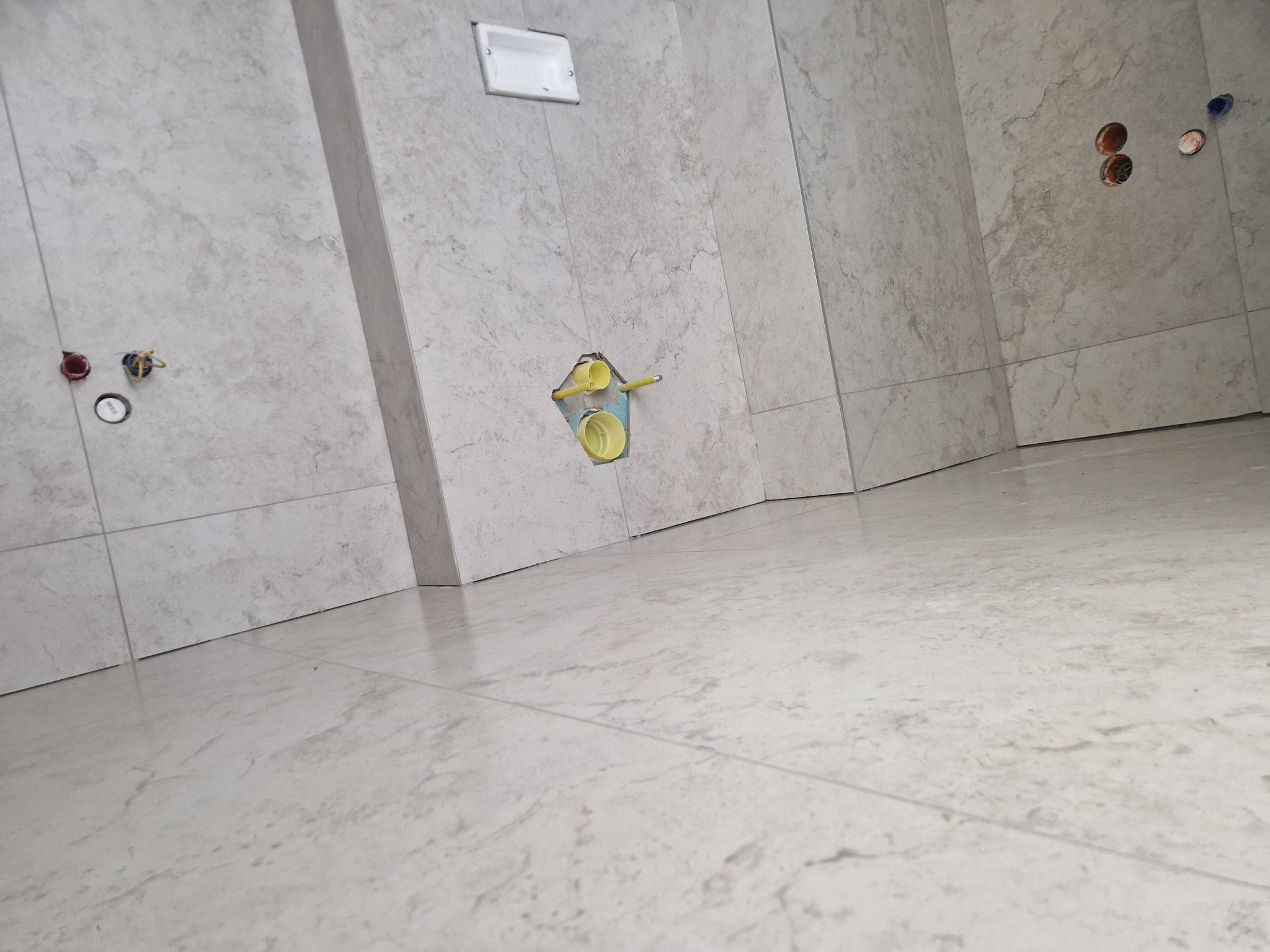 Ściany i podłoga wyłożone jasnymi płytkami w Cisiecu. Widoczne przygotowane punkty instalacyjne, w tym rury i kable, gotowe do dalszych prac wykończeniowych.