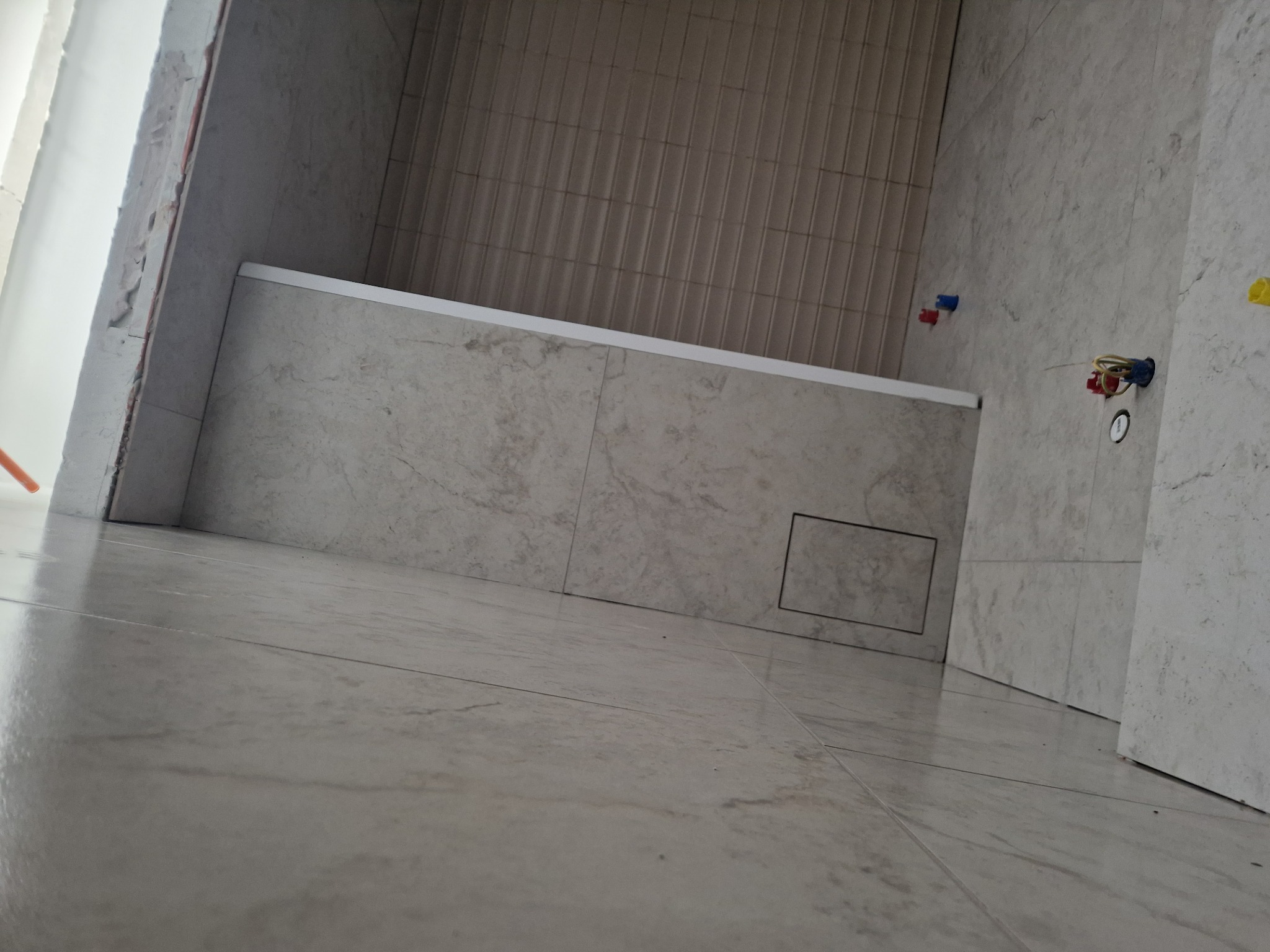 Wykończona łazienka z beżowymi płytkami na podłodze i ścianach, widoczna wanna i instalacja wodno-kanalizacyjna. Ujęcie z niskiego kąta podkreśla przestrzeń.