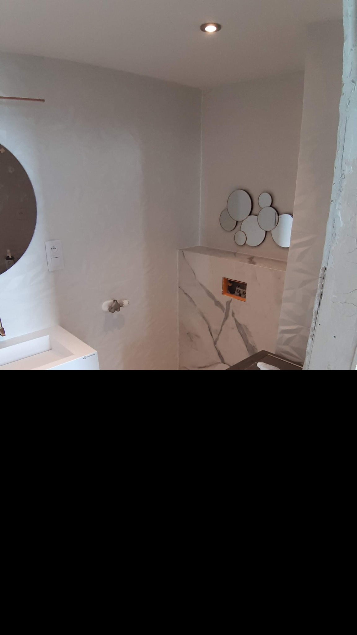 Nowoczesna łazienka z umywalką nablatową, okrągłym lustrem i dekoracyjnymi lustrami na ścianie z płytek imitujących marmur, widoczna instalacja podtynkowa.