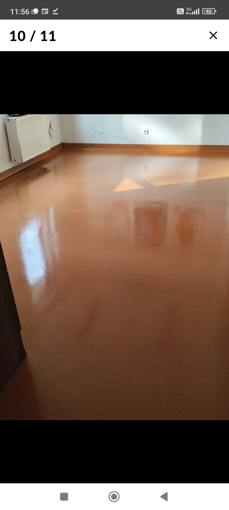 Błyszcząca, świeżo umyta podłoga w pokoju z grzejnikiem i jasnymi ścianami. Widoczne refleksy światła podkreślają czystość powierzchni.