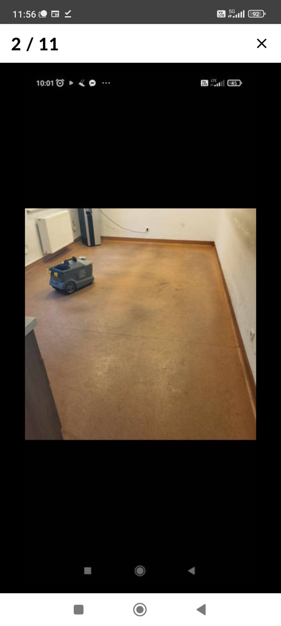 Automat do mycia podłóg na brązowej, matowej posadzce w pustym pomieszczeniu biurowym, widoczny grzejnik i listwy przypodłogowe.