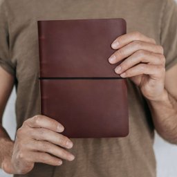 MokVok Sp. z O.O. - Osoba trzyma w dłoniach brązowy, skórzany notatnik z czarną gumką zamykającą.
