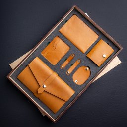 MokVok Sp. z O.O. - Zestaw galanterii skórzanej w odcieniach karmelowego brązu, zawierający portfel kopertowy, etui na karty, notes, mały portfelik i uchwyty na kable, umieszczony w drewnianym pudełku z szarą wkładką...