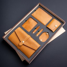 MokVok Sp. z O.O. - Zestaw galanterii skórzanej w drewnianym pudełku z szarą wkładką: portfel, etui na karty, okładka na dokumenty, mini portfel, uchwyty na kable. Wszystko w odcieniach brązu.