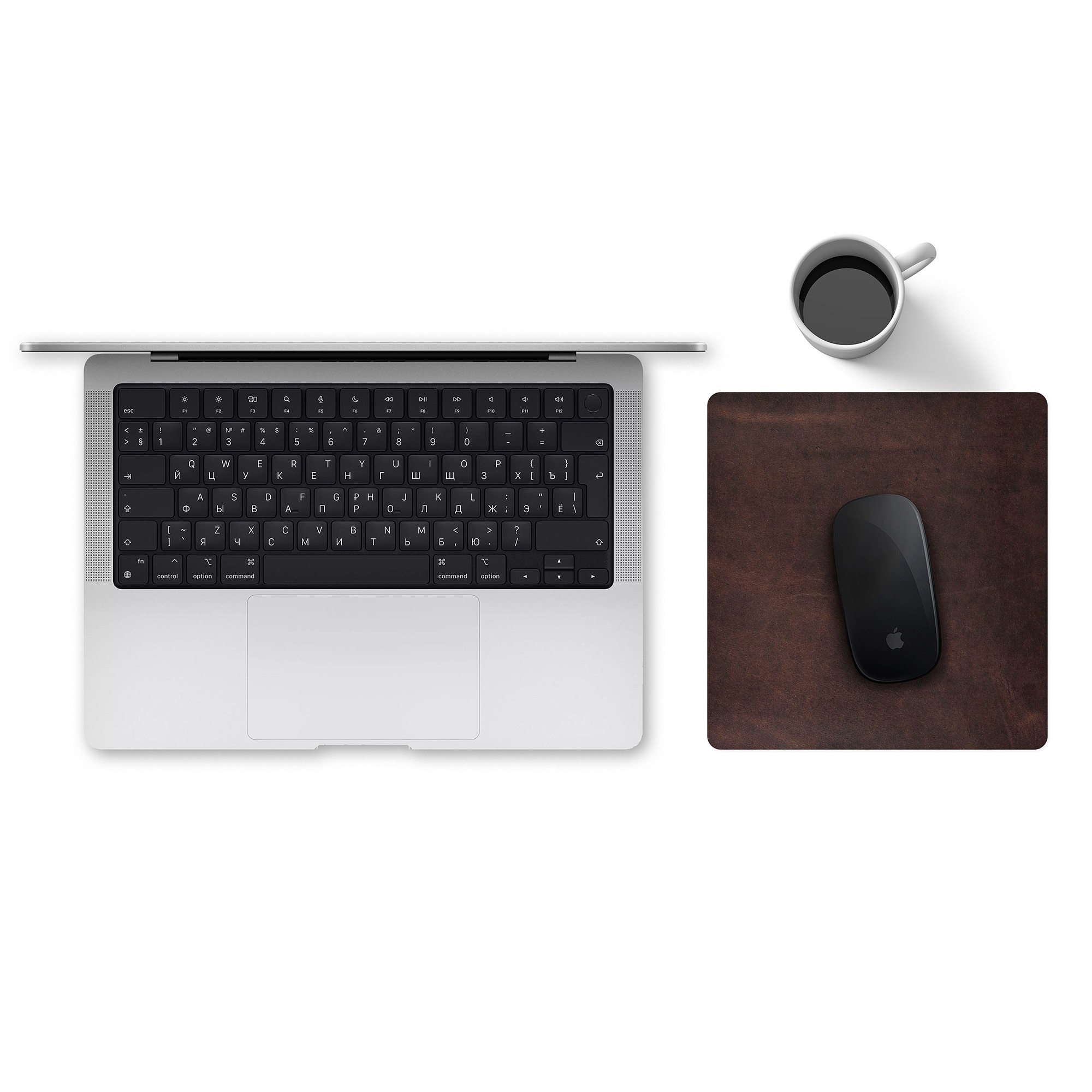 Widok z góry na srebrnego laptopa z czarną klawiaturą, biały kubek z czarną kawą i czarną myszkę na brązowej, skórzanej podkładce, umieszczone na białym biurku.