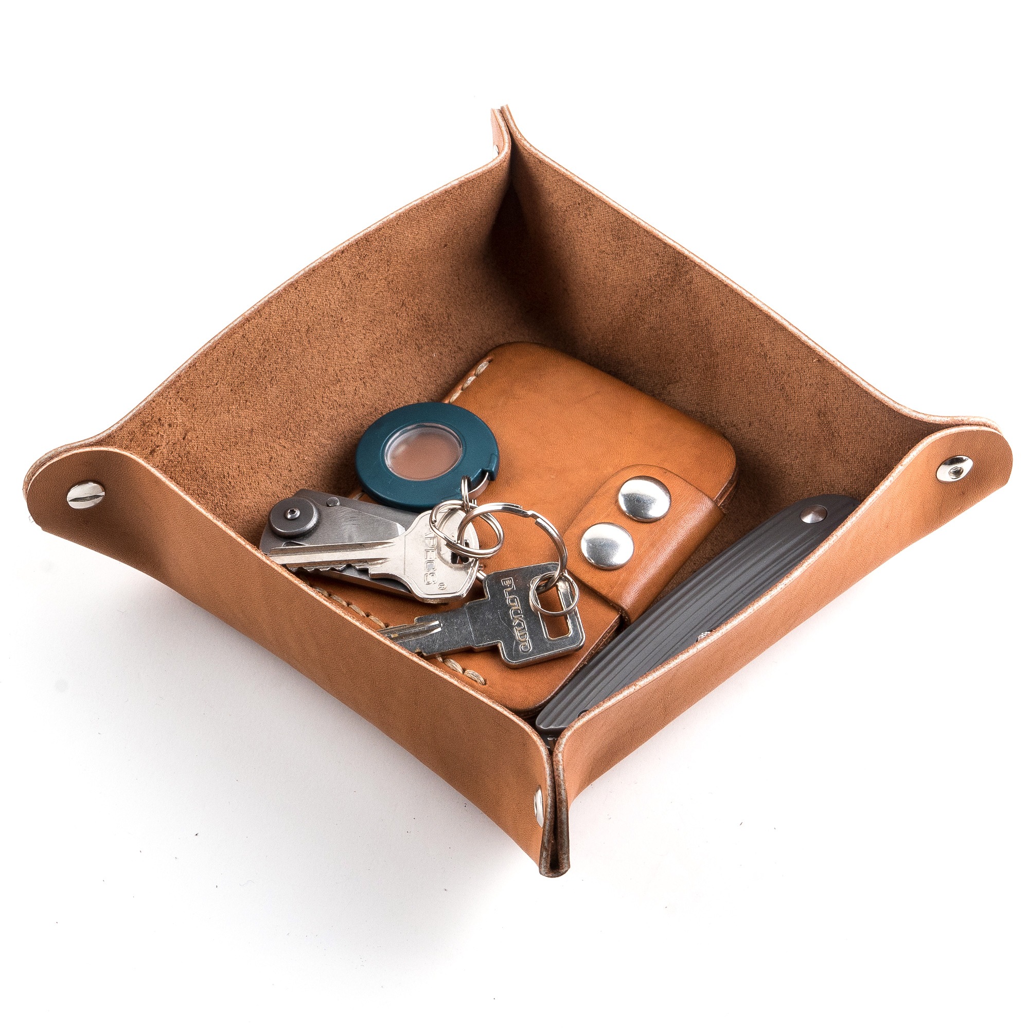 Kwadratowa, skórzana tacka organizer na drobiazgi w kolorze brązowym, wypełniona kluczami, portfelem i scyzorykiem, widok z góry na białym tle.