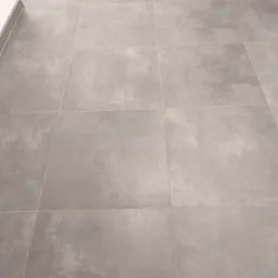 Szare, matowe płytki podłogowe ułożone w kwadraty z fugami, widoczne przy listwie przypodłogowej.