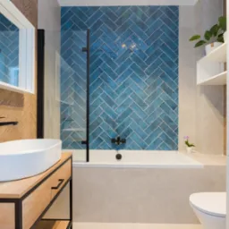 Nowoczesna łazienka z niebieską ścianą z płytek ułożonych w jodełkę, owalną umywalką na drewnianej szafce z czarnymi elementami, wanną z czarną armaturą i szklanym parawanem oraz wiszącą toaletą.