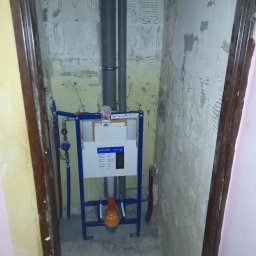 Renomo - Montaż stelaża podtynkowego WC Cersanit Tech Line z widocznymi rurami odpływowymi i dopływowymi, na tle surowej ściany w trakcie prac wykończeniowych łazienki.