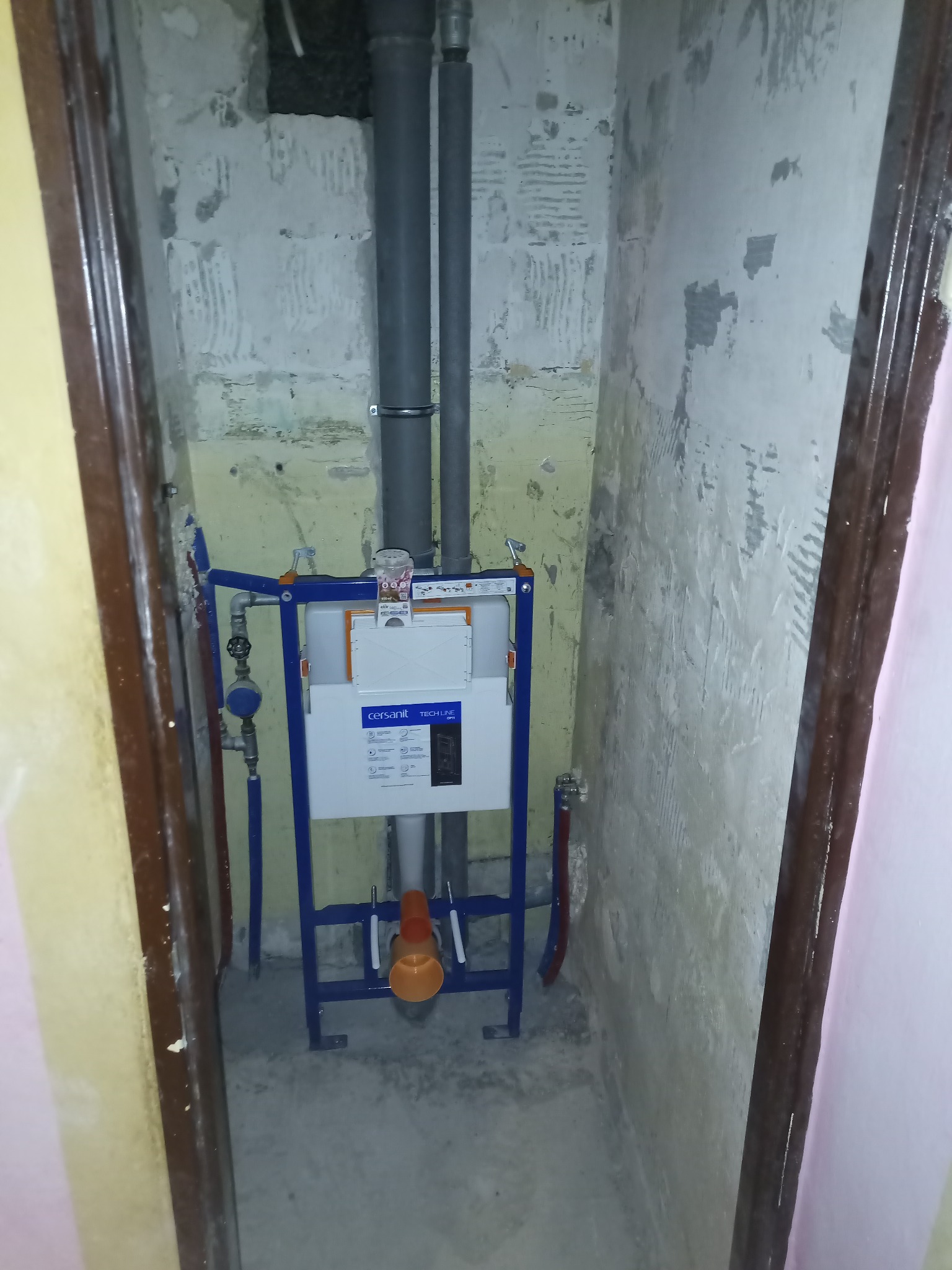 Montaż stelaża podtynkowego WC Cersanit Tech Line z widocznymi rurami odpływowymi i dopływowymi, na tle surowej ściany w trakcie prac wykończeniowych łazienki.