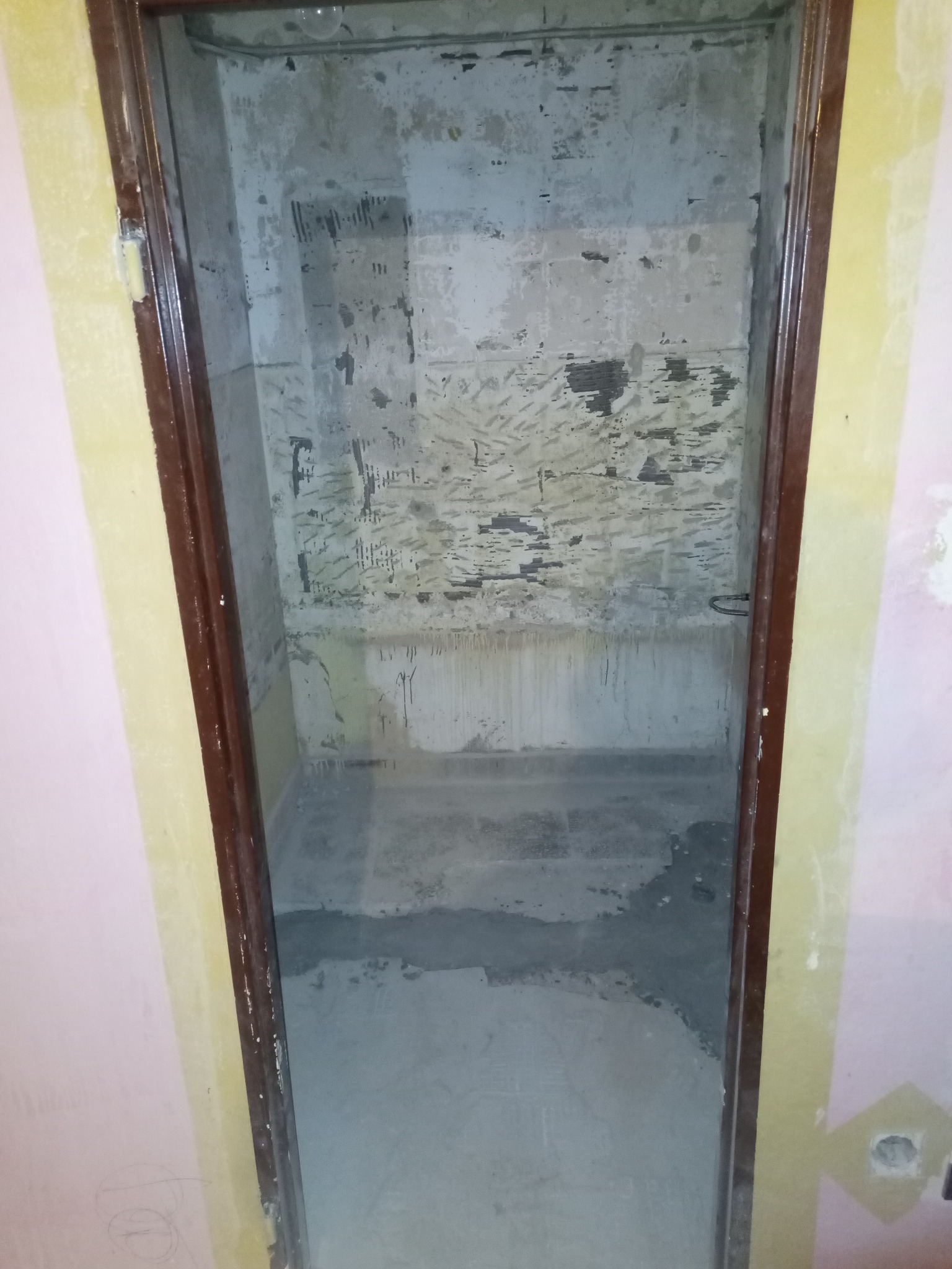 Łazienka w trakcie demontażu starych płytek i przygotowania podłoża, widoczne ślady po kleju i resztki starej okładziny na ścianach, częściowo wylany podkład na podłodze, ościeżnica drzwiowa...