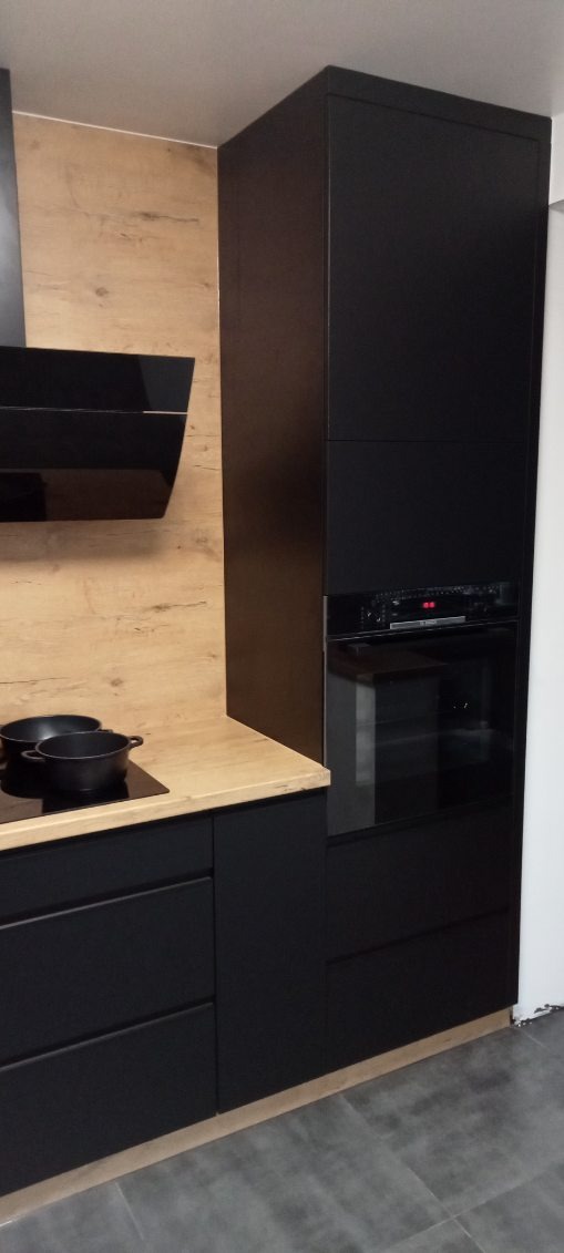 Część czarnej zabudowy kuchennej z piekarnikiem, blatem w kolorze drewna i dwoma czarnymi garnkami na płycie indukcyjnej.