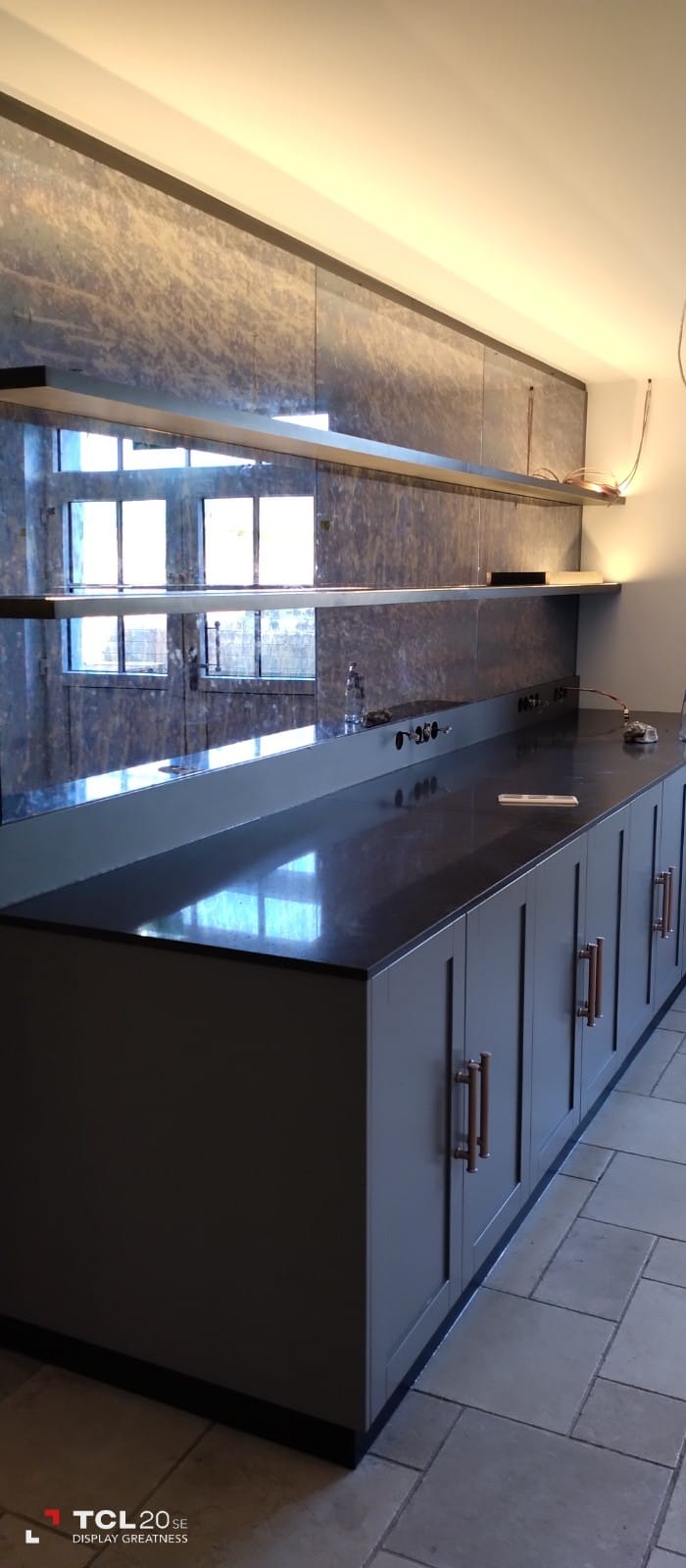 Nowoczesna kuchnia z szarymi szafkami, blatem z ciemnego kamienia i marmurowym panelem na ścianie, oświetlona listwą LED pod półkami.