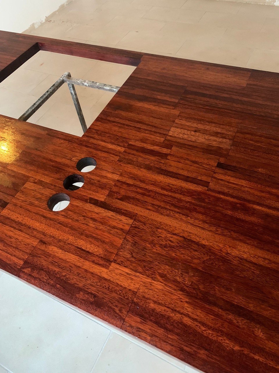 Błyszczący, nowo położony parkiet z egzotycznego drewna z wyciętymi otworami na kable i otworem na instalację, widoczne fragmenty podłogi z płytek.