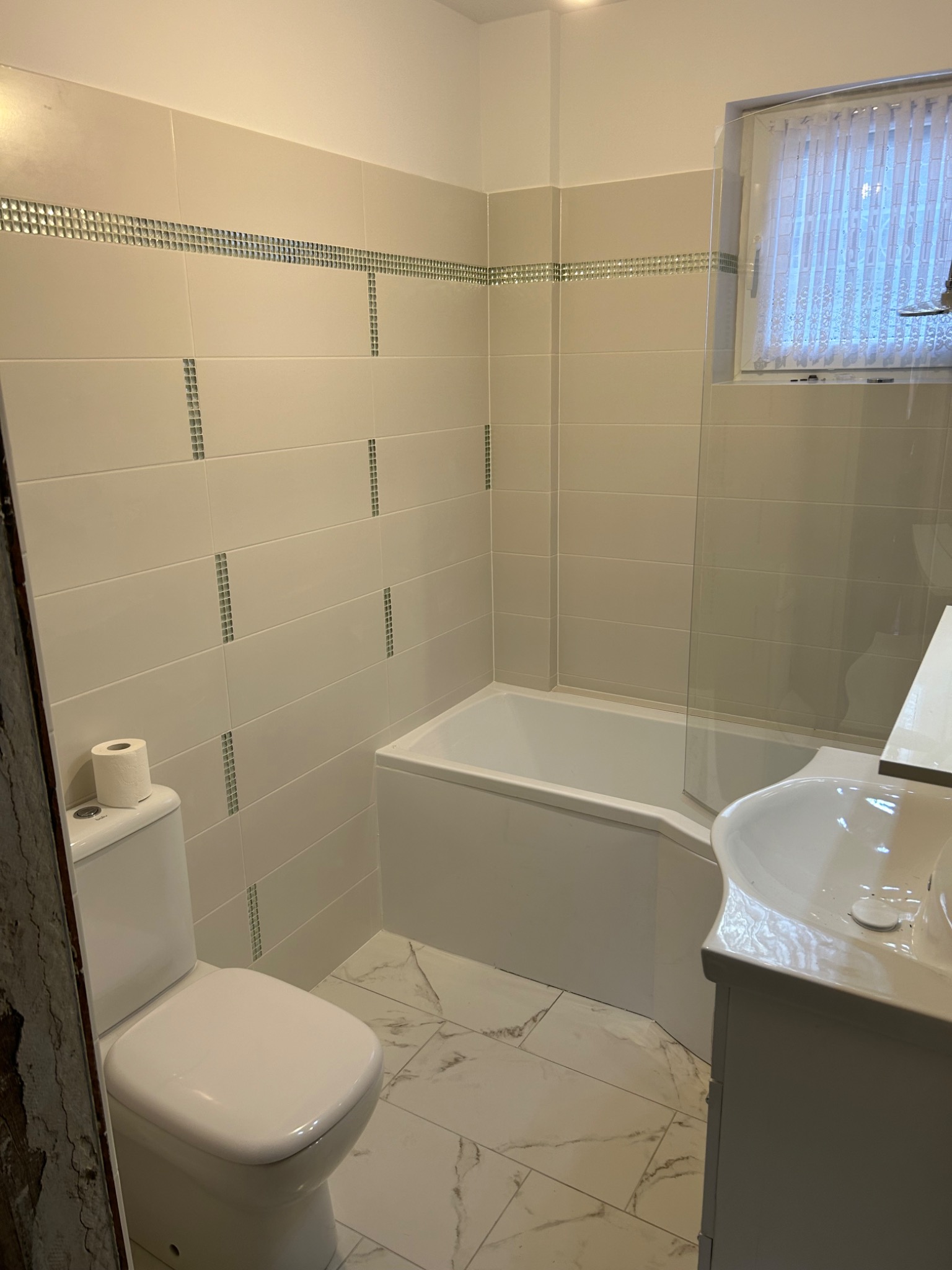 Jasna łazienka po remoncie z wanną, umywalką i toaletą, wykończona płytkami z dekoracyjnymi wstawkami, marmurowa podłoga.