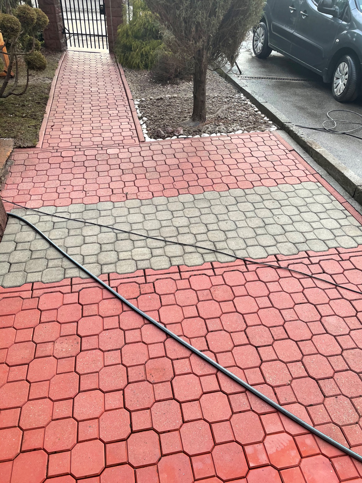 Czerwono-szara kostka brukowa ułożona na podjeździe, z widocznym kablem leżącym na powierzchni.