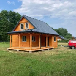 Nowoczesny dom szkieletowy z drewnianą elewacją i ciemnym dachem w Wejherowie, z widocznym czerwonym samochodem dostawczym w tle.