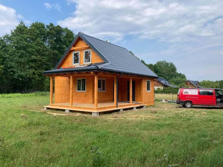 Nowoczesny dom szkieletowy z drewnianą elewacją i ciemnym dachem w Wejherowie, z widocznym czerwonym samochodem dostawczym w tle.