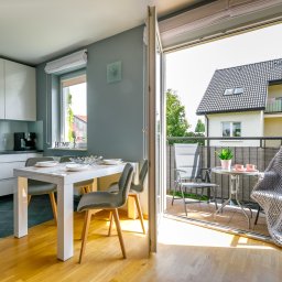 DOMUS NIERUCHOMOŚCI HANNA MORAWSKA - Nowoczesne wnętrze mieszkania z otwartą kuchnią, jadalnią i balkonem z widokiem na dom jednorodzinny.