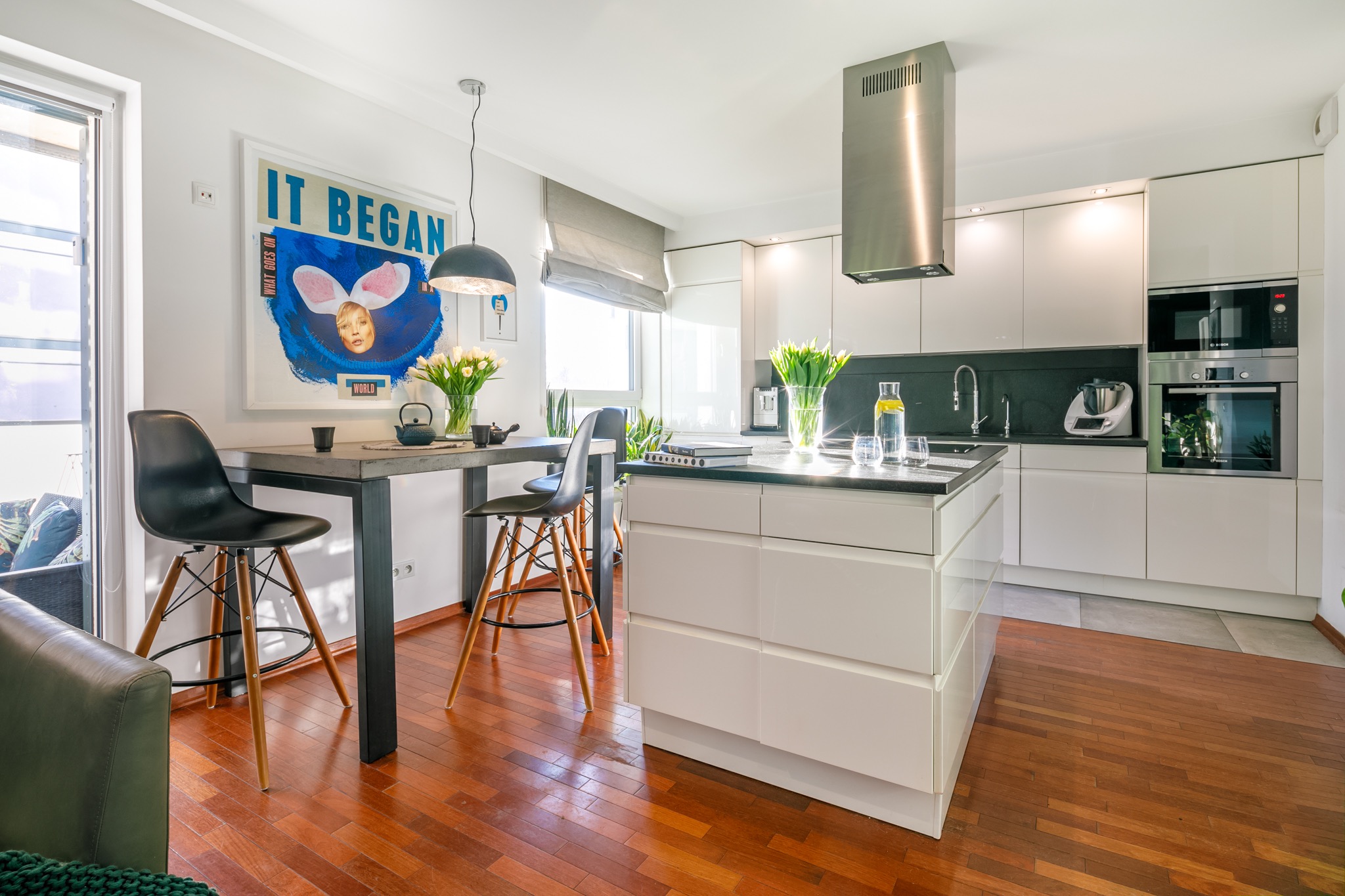 Jasna, nowoczesna kuchnia z wyspą, drewnianą podłogą i plakatem z królikiem na ścianie.