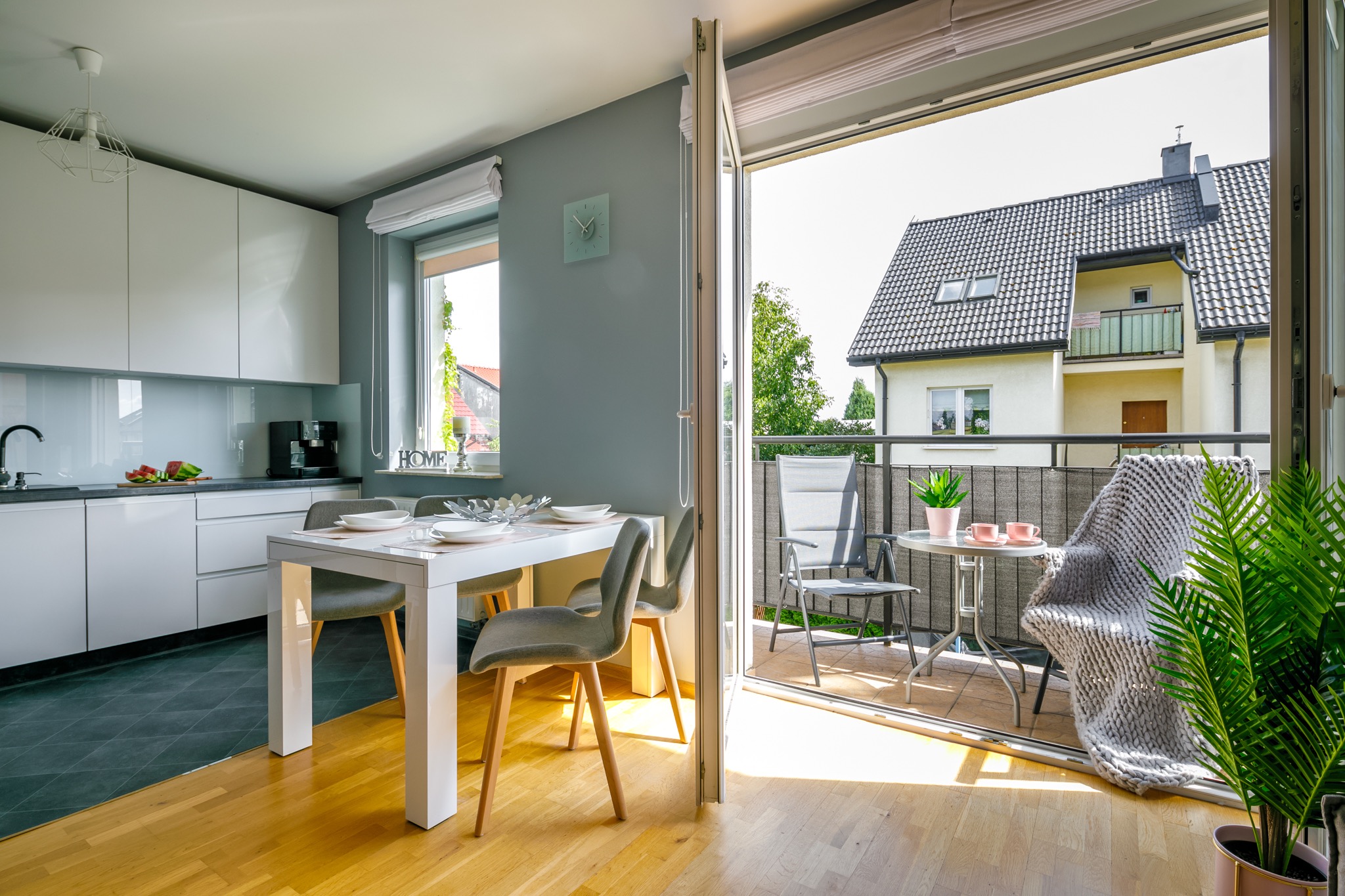 Nowoczesne wnętrze mieszkania z otwartą kuchnią, jadalnią i balkonem z widokiem na dom jednorodzinny.