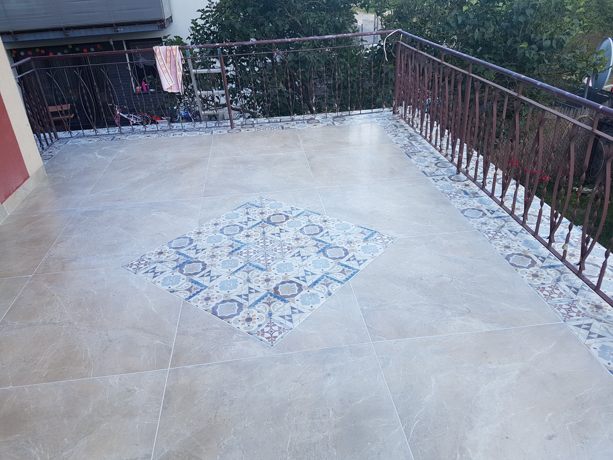 Wykończony balkon w Gdyni z beżowymi płytkami imitującymi marmur i dekoracyjnym, kwadratowym wzorem z płytek w centrum oraz ozdobnym pasem płytek pod metalową barierką.