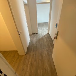 Daniel Obszyński - Korytarz z nową podłogą w odcieniach brązu, widoczne fragmenty niedokończonego wykończenia przy ścianach i drzwiach.