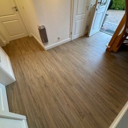 Daniel Obszyński - Nowa podłoga z paneli w odcieniach drewna, widok na białe drzwi i fragment drabiny w tle.