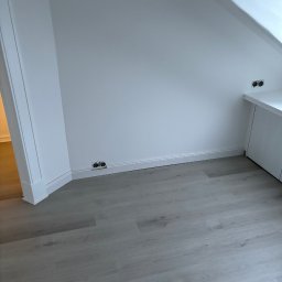 Daniel Obszyński - Jasnoszare panele podłogowe ułożone w pokoju ze skosami, widoczne gniazdka elektryczne przy podłodze i białe listwy przypodłogowe.