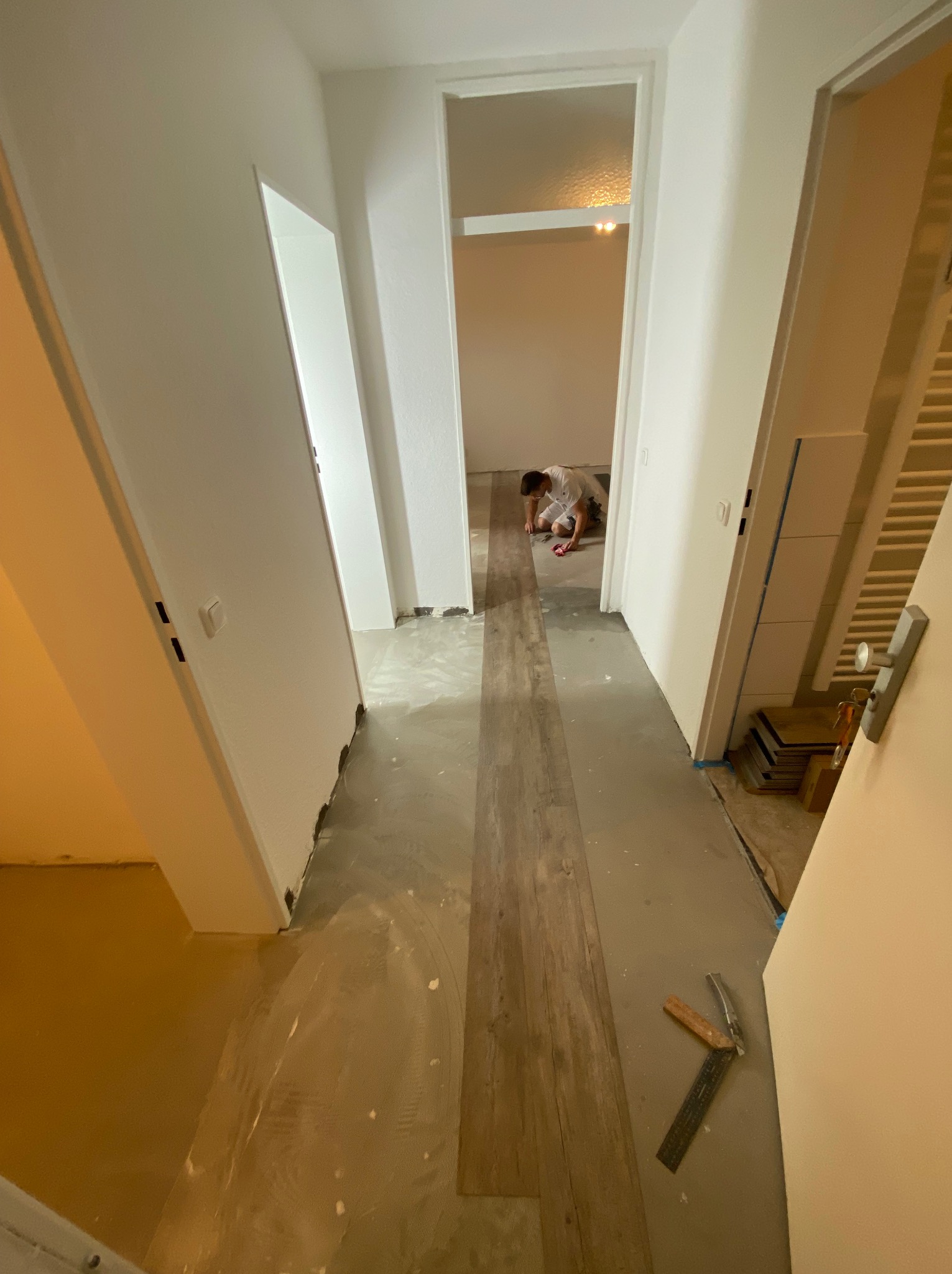 Układanie paneli podłogowych w mieszkaniu w Koszalinie, widoczne narzędzia glazurnicze i częściowo ułożone panele w korytarzu, wykonawca w oddali przy pracy.