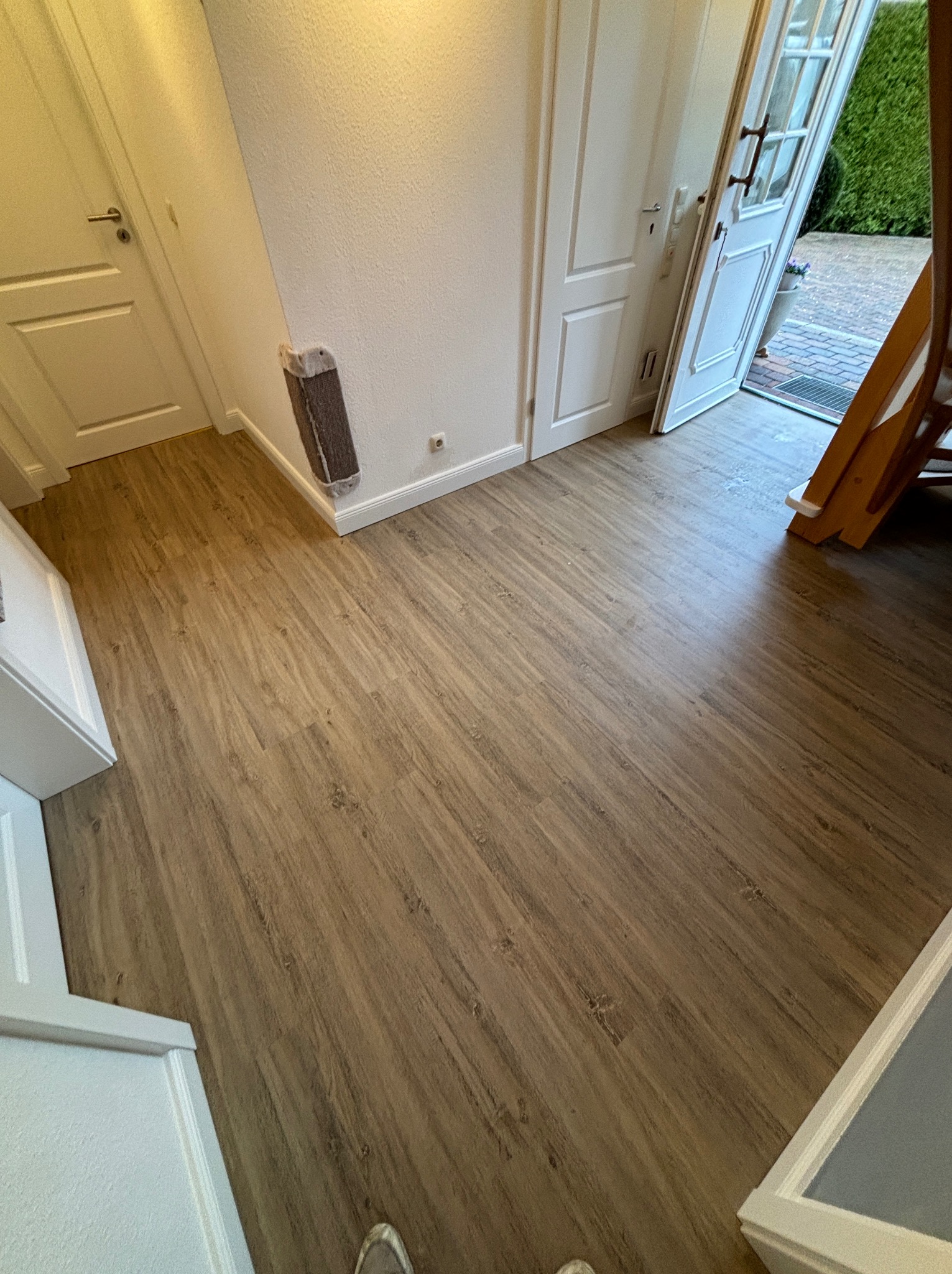 Nowa podłoga z paneli w odcieniach drewna, widok na białe drzwi i fragment drabiny w tle.
