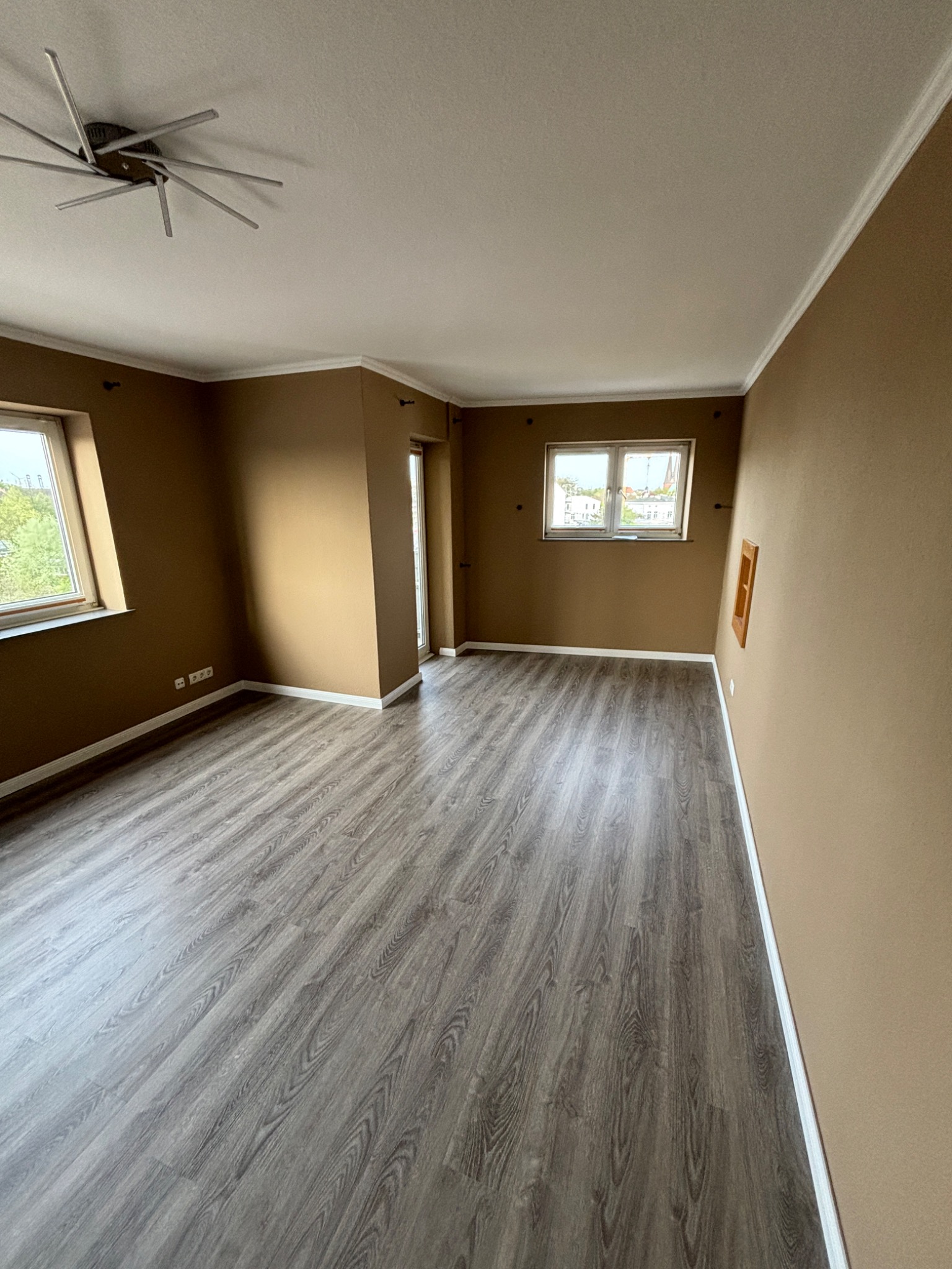 Nowo położona, szara podłoga z paneli w pustym pokoju w Koszalinie, z widokiem na miasto przez okno.