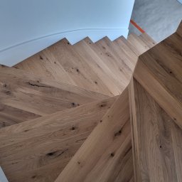 NORIX GM SPÓŁKA Z OGRANICZONĄ ODPOWIEDZIALNOŚCIĄ - Widok z góry na drewniane schody z wyraźnym usłojeniem i naturalnymi sękami, zabezpieczone niebieską taśmą malarską przy białej ścianie.