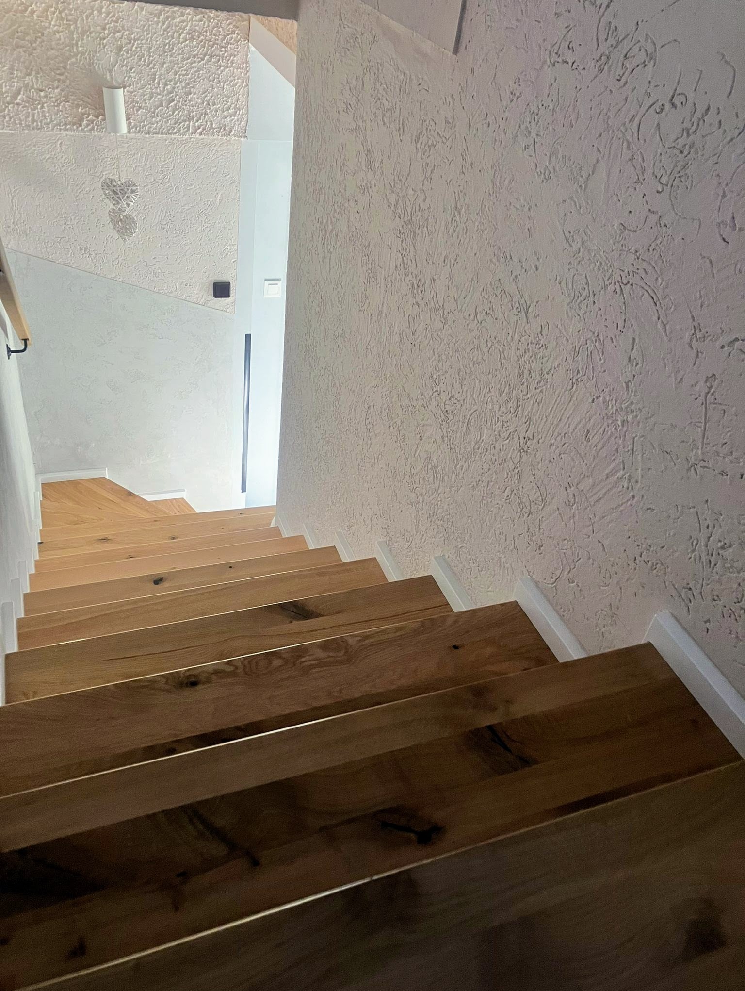 Nowoczesne schody z jasnego drewna, widok z góry, białe listwy przypodłogowe, ściana z dekoracyjnym tynkiem.