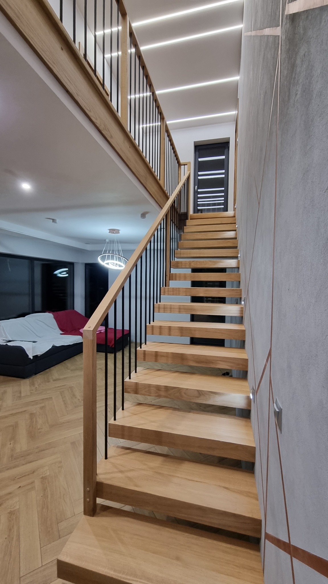 Nowoczesne, jasne stopnie z drewna z czarnymi metalowymi balustradami w dwupoziomowym mieszkaniu, widok z dołu na górę.