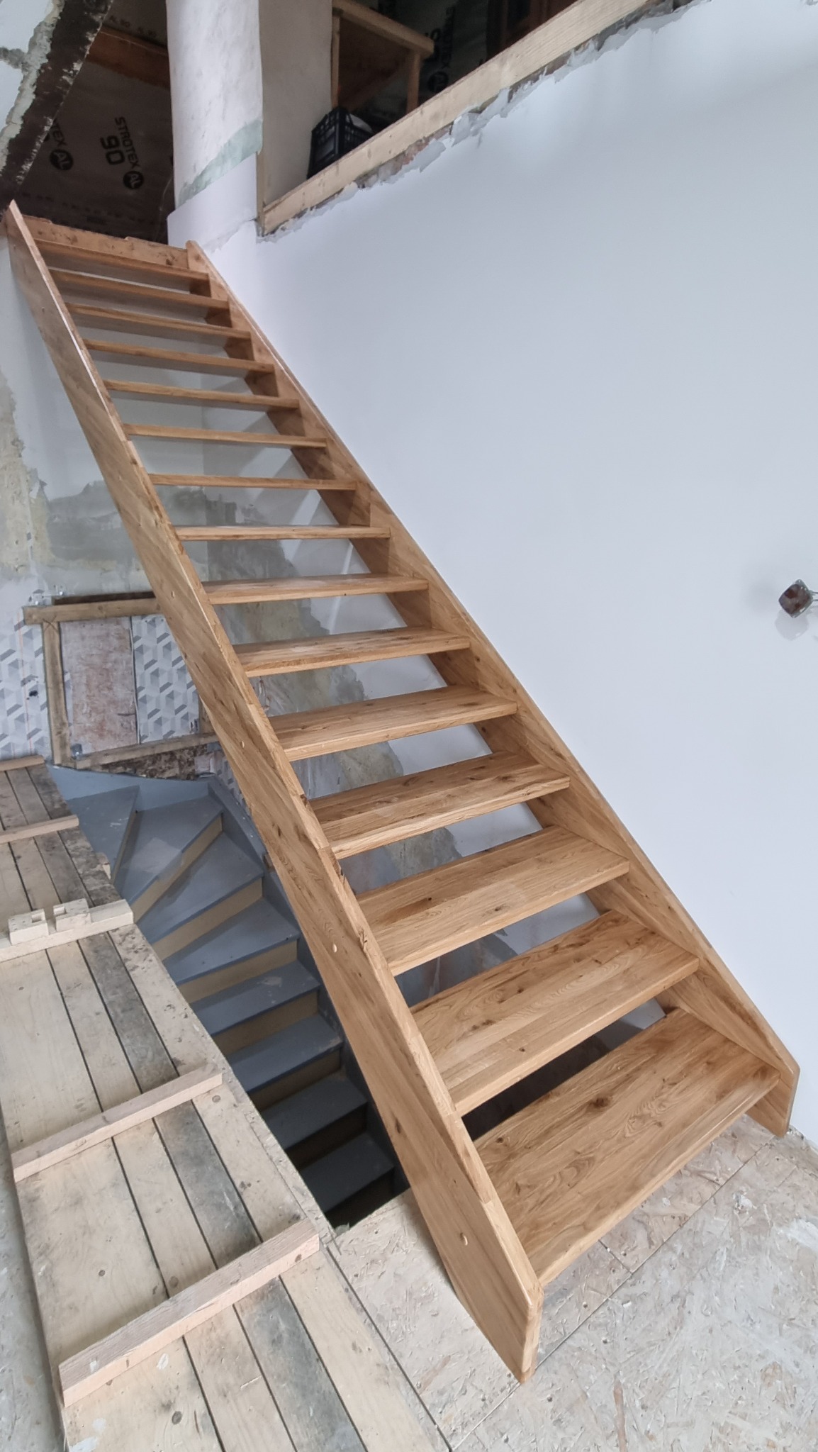 Surowe, jasne, ażurowe stopnie łączące kondygnacje w trakcie montażu, widoczne niedokończone wykończenia ścian i podłogi.