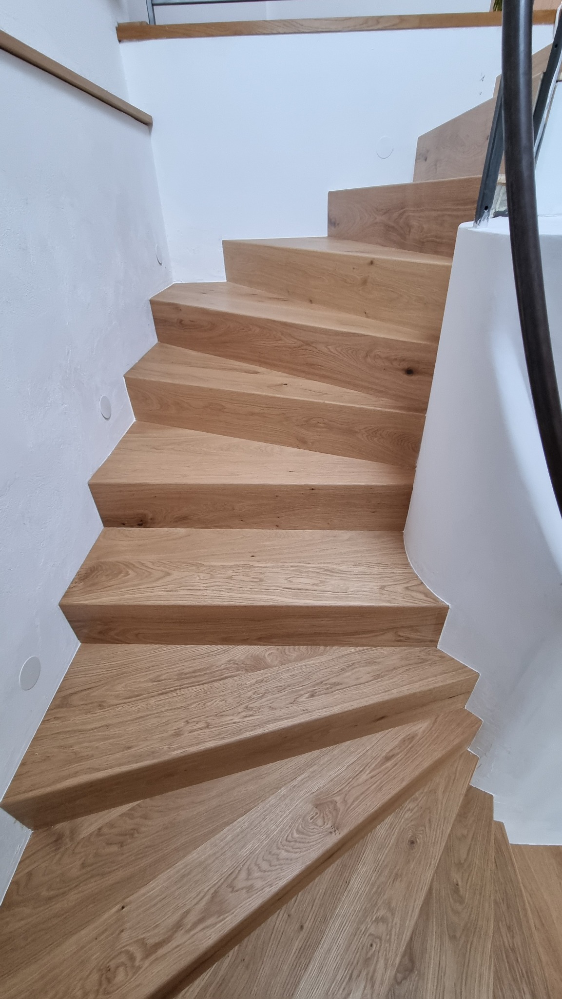 Spiralne schody z jasnego drewna z metalową poręczą, widok z góry, minimalistyczny design.